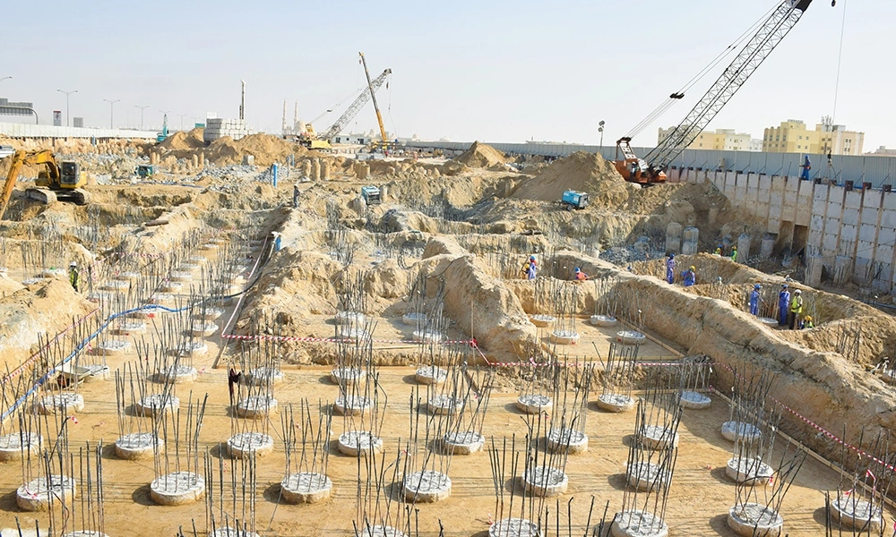 Large-scale bored pile foundation construction site in Dubai with exposed pile head rebar cages, shoring wall, and crawler cranes